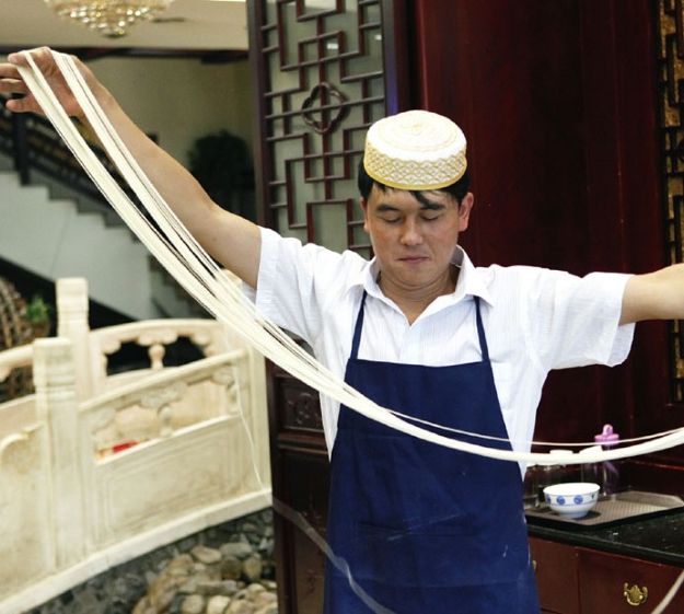 兰州牛肉面传统制作技艺——拉面师傅正在手工拉面，面团在手中飞舞成细条，展示百余年传承的精湛技艺