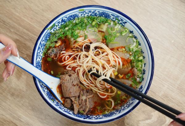一碗热气腾腾的兰州牛肉面特写，清澈的汤底、白色萝卜片、红色辣椒油、绿色香菜蒜苗、黄色面条，完美呈现一清二白三红四绿五黄