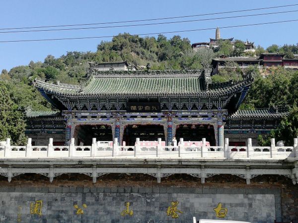 兰州白塔山公园山顶白塔近景，白色古塔矗立在绿树丛中，背景是蔚蓝天空和远处城市天际线